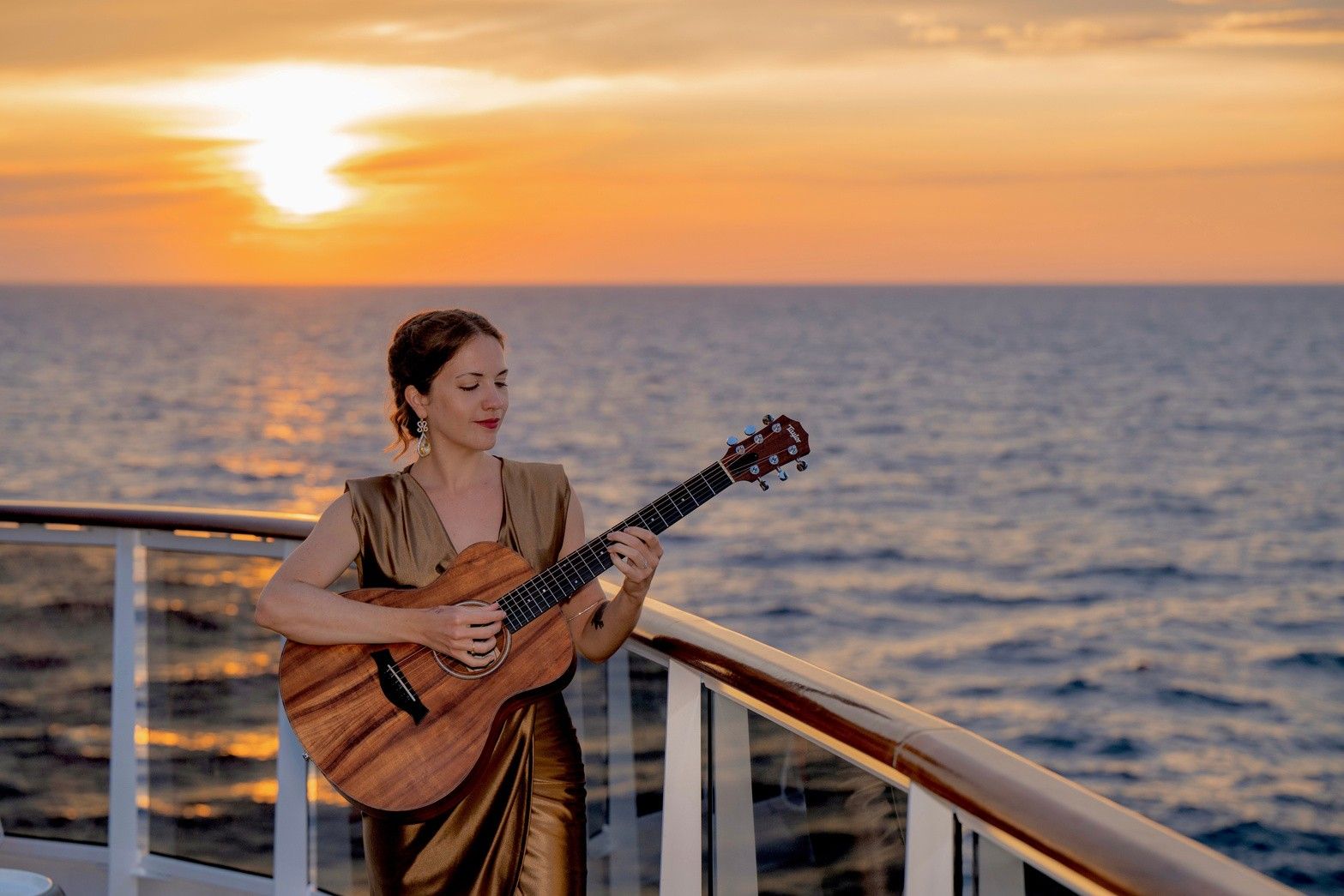 Lisette Luján tocando la guitarra en la cubierta de un crucero al atardecer